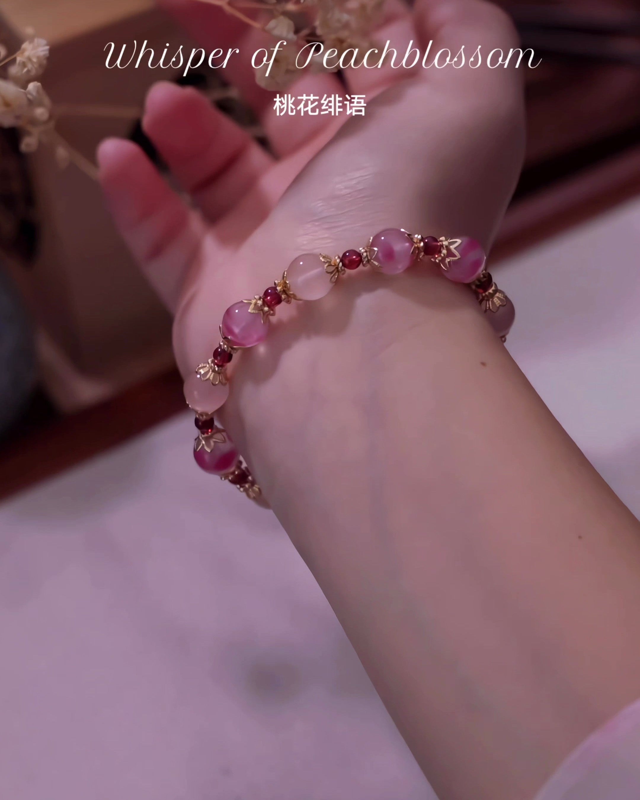 Hand wearing a pink beaded bracelet with 'Whisper of Peachblossom' text.